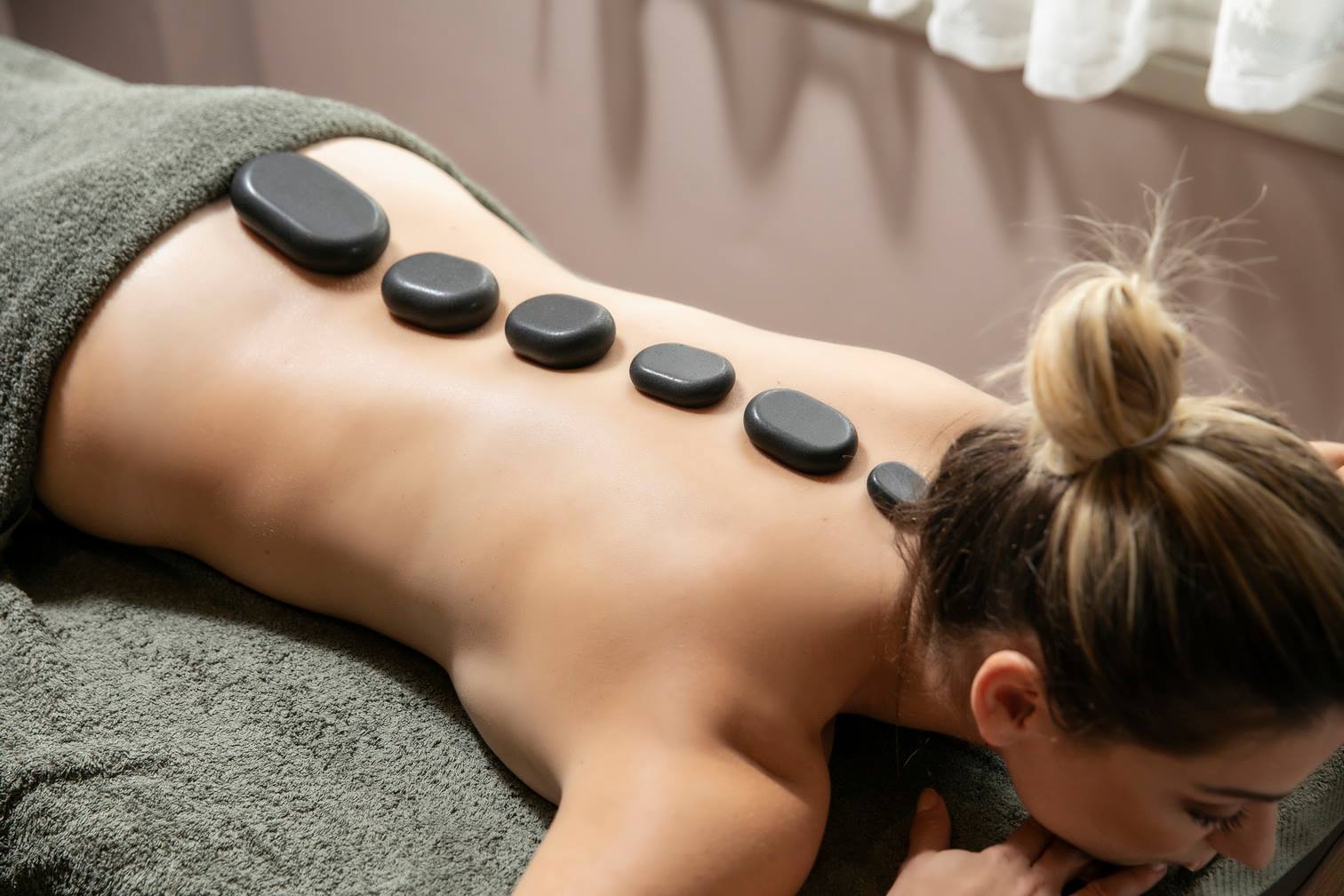 Ξαπλωμένη ξανθιά γυναίκα που της κάνουν hot stone μασάζ